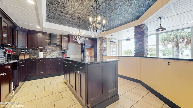 kitchen with dark stone countertops, hanging light fixtures, and wall chimney exhaust hood