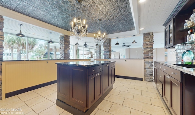 kitchen featuring a center island with sink, hanging light fixtures, dark brown cabinets, dark stone countertops, and ceiling fan