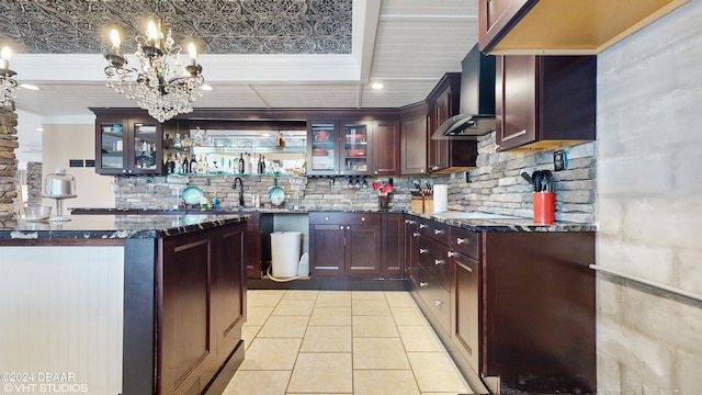 kitchen with wall chimney exhaust hood, hanging light fixtures, light tile patterned floors, dark stone countertops, and backsplash