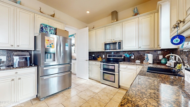 kitchen with sink, decorative backsplash, dark stone counters, light tile patterned floors, and stainless steel appliances