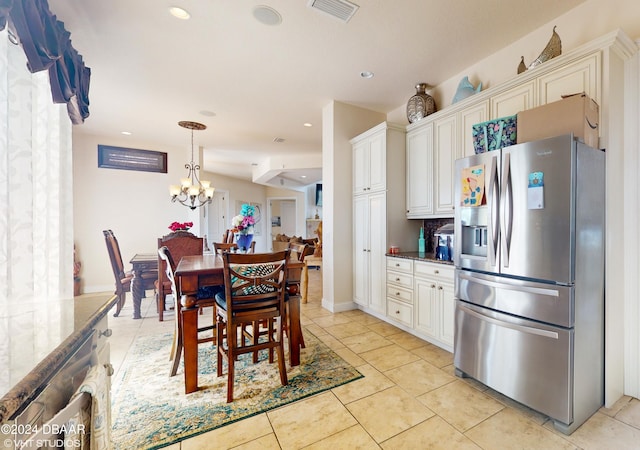 kitchen featuring white cabinetry, stainless steel fridge, decorative light fixtures, and dark stone countertops