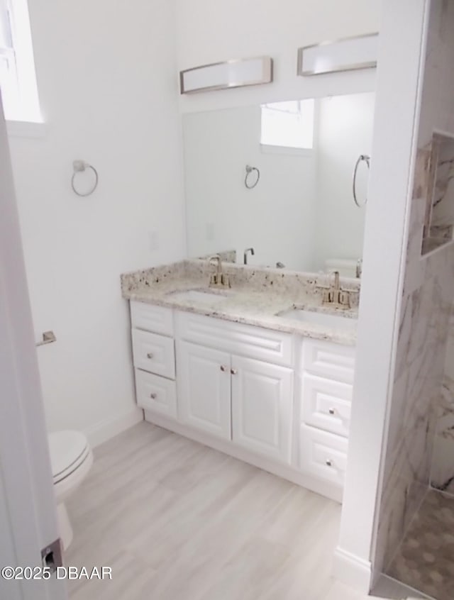 bathroom featuring double vanity, a marble finish shower, a sink, and toilet