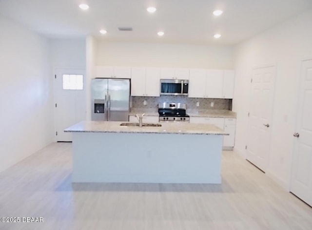 kitchen with a kitchen island with sink, stainless steel appliances, a sink, white cabinetry, and decorative backsplash