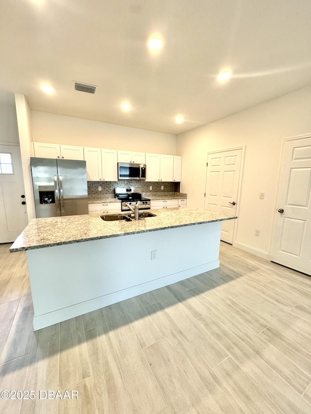 kitchen with a large island, light wood finished floors, stainless steel appliances, tasteful backsplash, and a sink