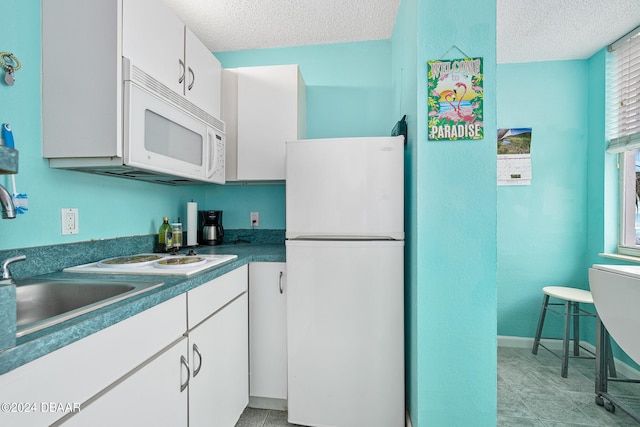 kitchen with white appliances, white cabinetry, light tile patterned floors, and a textured ceiling