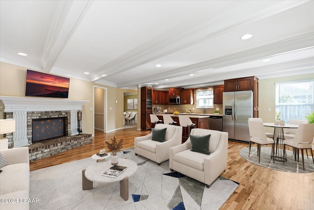 living room with beamed ceiling, light wood-type flooring, ornamental molding, and a brick fireplace