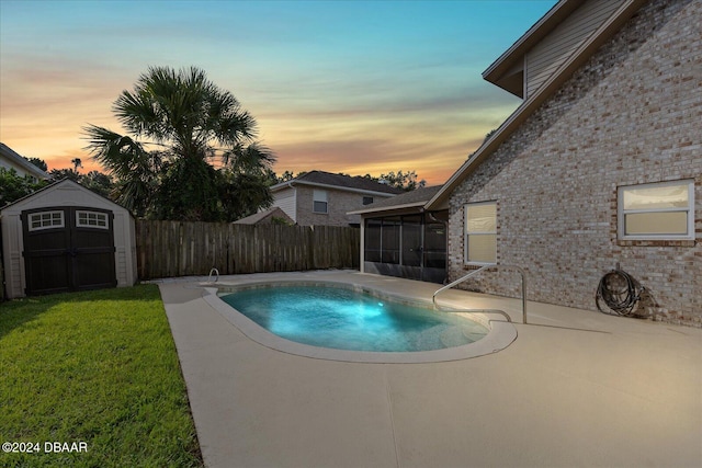 pool at dusk with a yard, a patio, and a storage shed