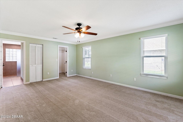 unfurnished bedroom with light carpet, connected bathroom, multiple windows, and ceiling fan