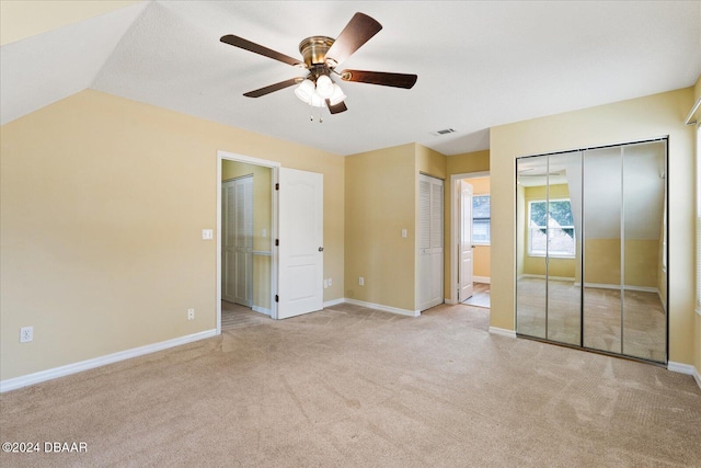 unfurnished bedroom with ceiling fan, ensuite bathroom, light colored carpet, and vaulted ceiling