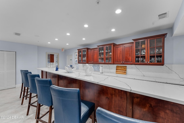 kitchen with light stone countertops, kitchen peninsula, backsplash, and a kitchen breakfast bar