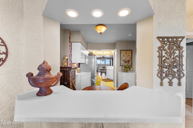 interior space with white cabinetry, kitchen peninsula, light tile patterned floors, and stainless steel fridge