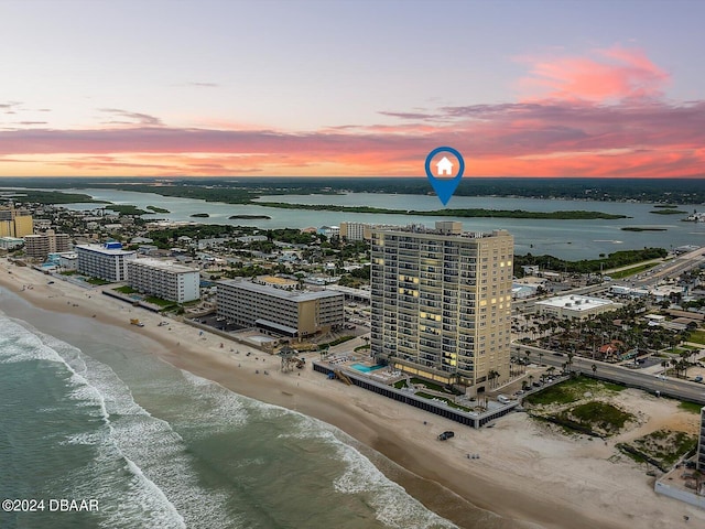 aerial view at dusk featuring a water view and a view of the beach