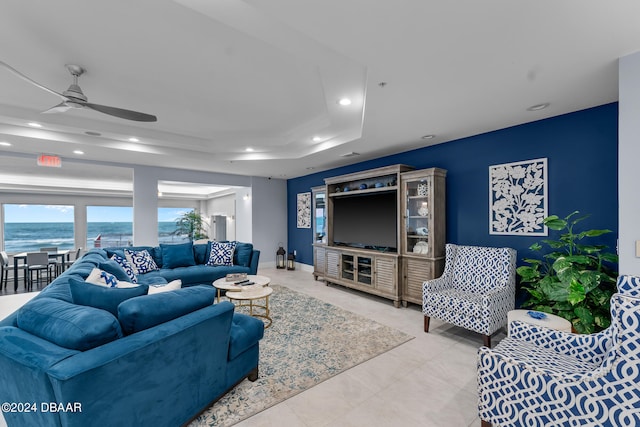 living room featuring a water view, ceiling fan, and a tray ceiling