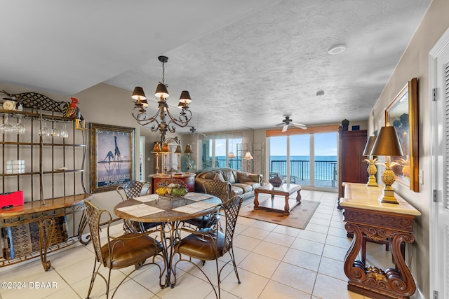 tiled dining area with ceiling fan with notable chandelier, a water view, and a textured ceiling