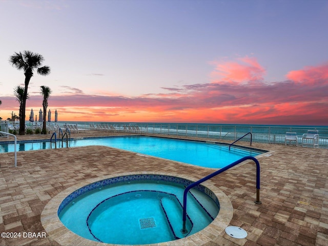 pool at dusk featuring a community hot tub, a water view, and a patio