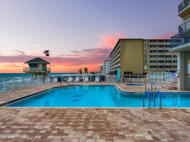 pool at dusk with a water view and a patio