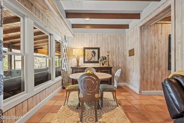 tiled dining room featuring beam ceiling, wooden walls, and a textured ceiling