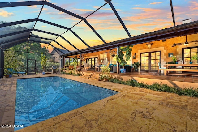 pool at dusk with a lanai, ceiling fan, and a patio area