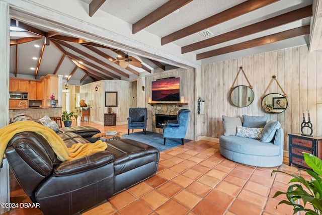 tiled living room with a stone fireplace, wooden walls, sink, and vaulted ceiling with beams