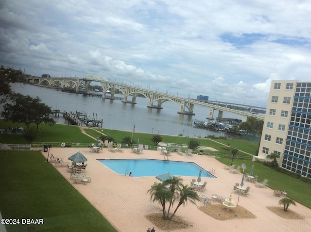 view of swimming pool featuring a lawn, a water view, and a patio area