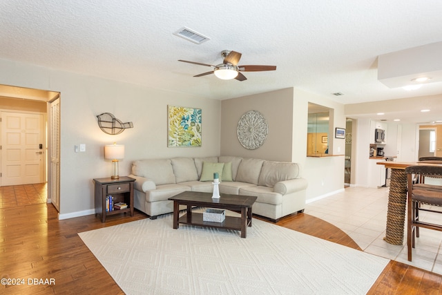 living room featuring ceiling fan, light hardwood / wood-style floors, and a textured ceiling