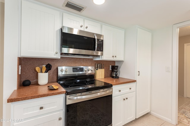 kitchen with appliances with stainless steel finishes, light tile patterned floors, white cabinetry, and backsplash