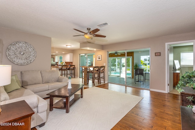 living room with hardwood / wood-style flooring, ceiling fan, and a textured ceiling