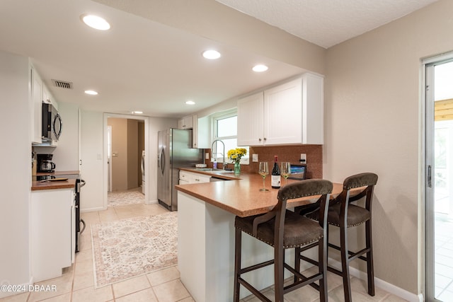 kitchen featuring white cabinetry, a breakfast bar, light tile patterned floors, and stainless steel appliances