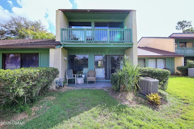 rear view of house with a yard, a balcony, central AC unit, and a patio