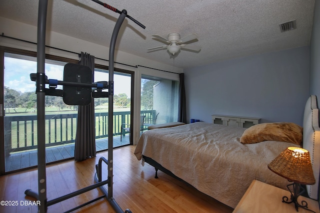 bedroom with a textured ceiling, access to exterior, hardwood / wood-style floors, and ceiling fan