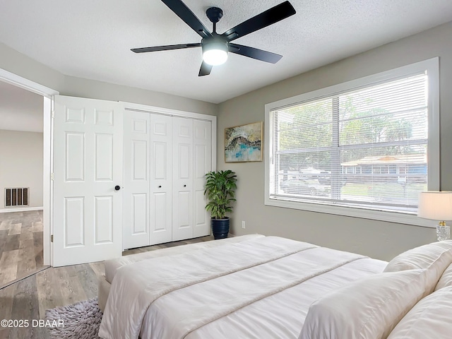 bedroom with visible vents, a closet, wood finished floors, a textured ceiling, and a ceiling fan