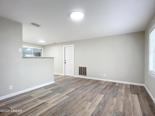 empty room featuring baseboards, visible vents, a wealth of natural light, and wood finished floors