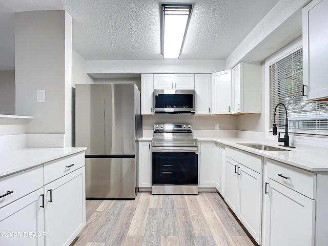 kitchen featuring light wood-type flooring, a textured ceiling, white cabinets, a sink, and appliances with stainless steel finishes