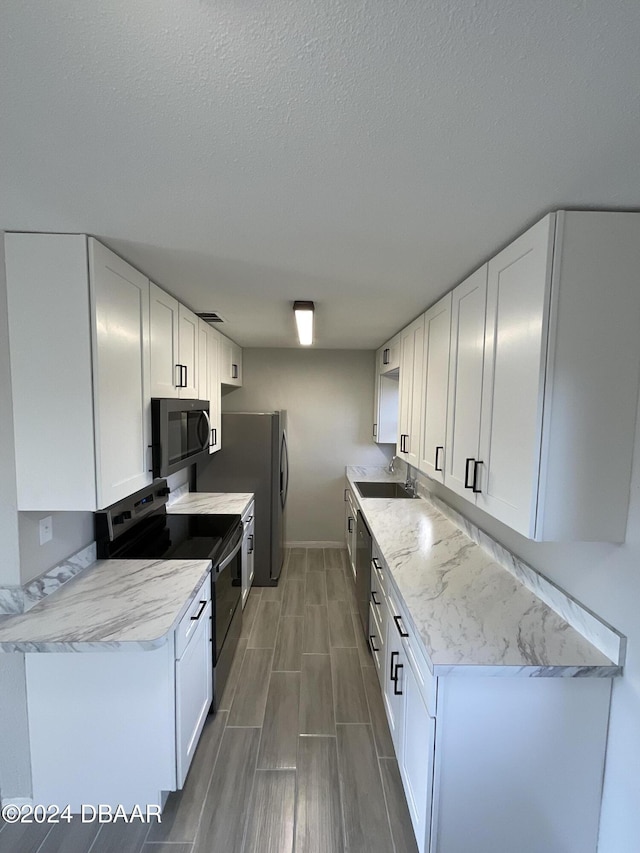 kitchen with appliances with stainless steel finishes, dark hardwood / wood-style floors, white cabinetry, and sink