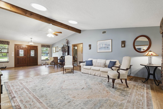 living room with ceiling fan, vaulted ceiling with beams, wood-type flooring, and a textured ceiling