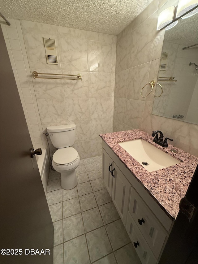 bathroom featuring tile walls, vanity, a textured ceiling, tile patterned floors, and toilet