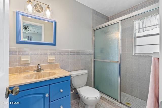 bathroom featuring toilet, vanity, tile walls, and a shower with door