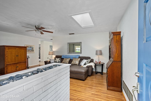 living room featuring ceiling fan, light wood-type flooring, and a skylight