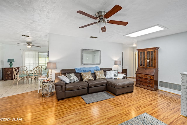 living room with a brick fireplace, light hardwood / wood-style floors, a textured ceiling, and ceiling fan