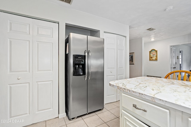 kitchen with white cabinets, stainless steel refrigerator with ice dispenser, light stone counters, and light tile patterned flooring