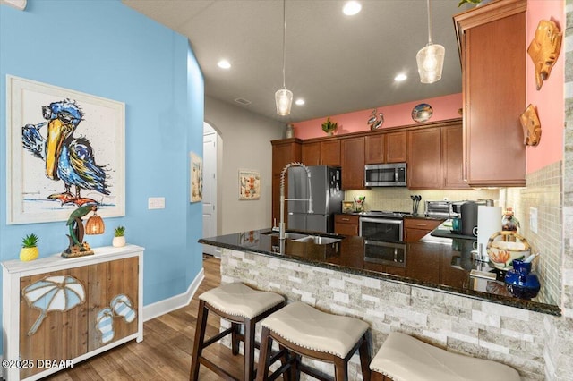 6341 Hanfield Dr, Port Orange, FL 32128 - kitchen featuring arched walkways, a peninsula, brown cabinetry, wood finished floors, and stainless steel appliances
