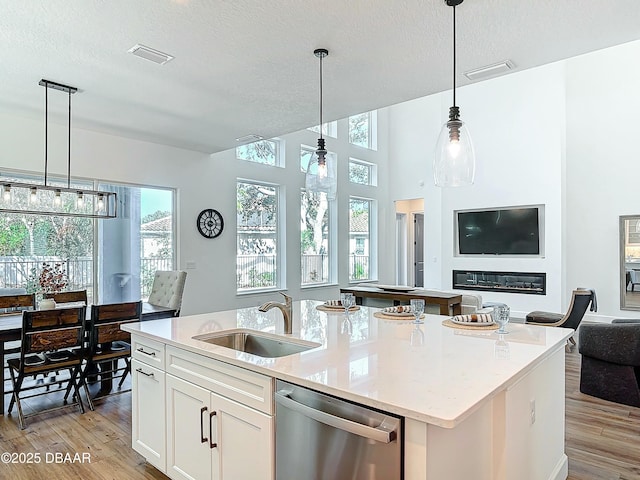 kitchen featuring sink, white cabinets, a center island with sink, stainless steel dishwasher, and light wood-type flooring