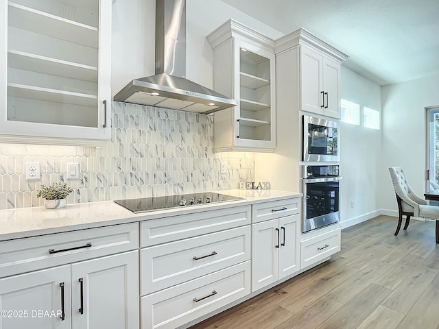 kitchen featuring wall chimney range hood, backsplash, white cabinets, black electric cooktop, and stainless steel oven