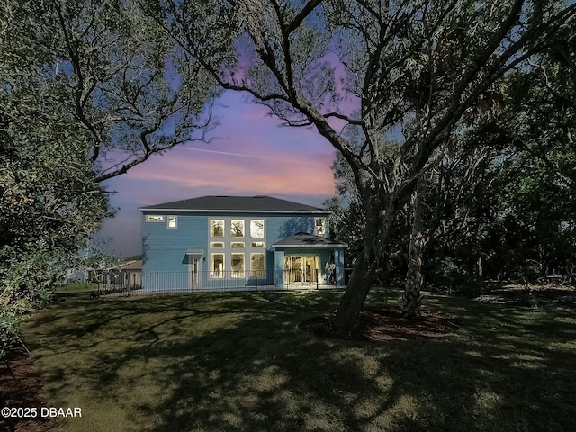 back house at dusk featuring a lawn