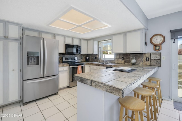 kitchen with a breakfast bar, stainless steel appliances, tile counters, backsplash, and a peninsula