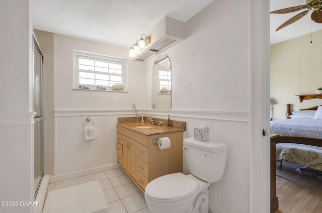 full bath with ensuite bathroom, tile patterned flooring, a shower with shower door, toilet, and a wainscoted wall