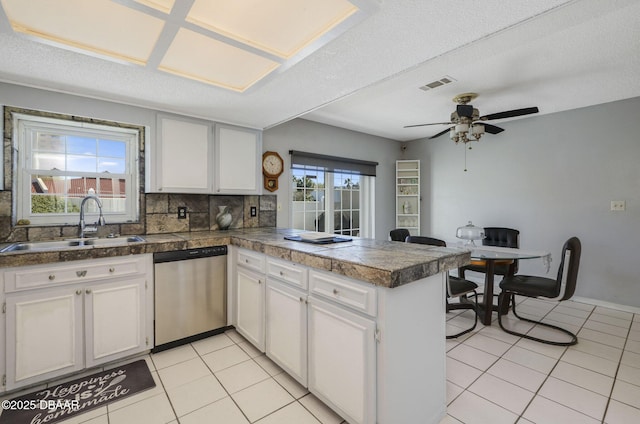 kitchen with tile countertops, a peninsula, stainless steel dishwasher, and a sink