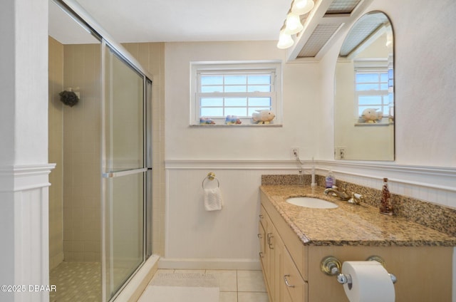 bathroom featuring a stall shower, tile patterned flooring, a wainscoted wall, and vanity