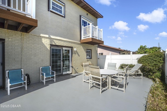 view of patio with outdoor dining space, fence, and a balcony