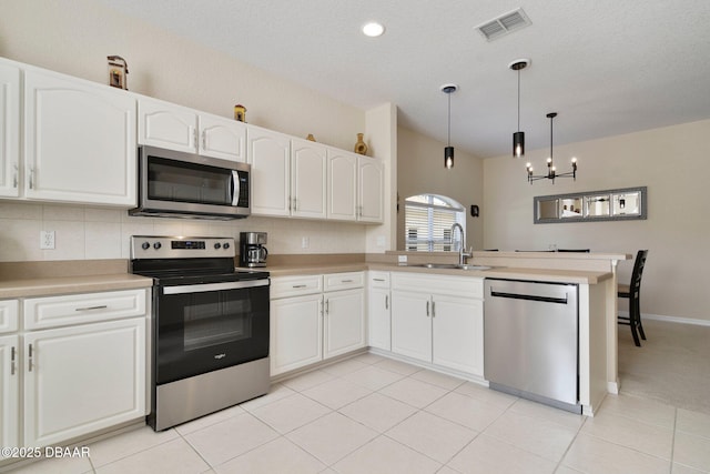 kitchen with appliances with stainless steel finishes, decorative light fixtures, white cabinetry, sink, and kitchen peninsula